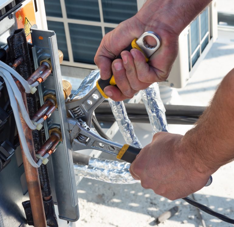 Un technicien CVC travaille sur des unités de climatisation sur le toit d'un nouveau bâtiment industriel. Le technicien utilise une clé fixe pour serrer l'unité extérieure de climatisation. L'homme tient une clé à la main.